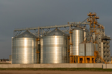 silver silos on agro manufacturing plant for processing drying cleaning and storage of agricultural products, flour, cereals and grain. Large iron barrels of grain. Granary elevator