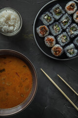 a bowl of tom yam soup, a jar of rice and a set of sushi. Top view