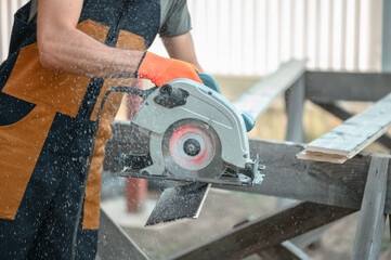A man in uniform makes a cut of the planking Board using a circular saw. Flying sawdust, shallow depth of field.