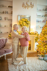 Senior couple dancing near christmas tree and feeling happy
