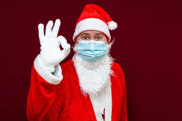 Santa Claus man wears face mask shows gesture ok. coronavirus covid-19 during quarantine.