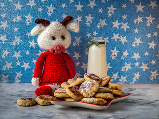 Children's breakfast with homemade cookies and milk in a glass bottle. Knitted bull calf in a red sweater
