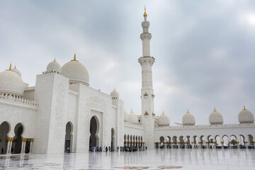 Fototapeta na wymiar Minaret and domes of white Grand Mosque against white cloudy sky, also called Sheikh Zayed Grand Mosque, inspired by Persian, Mughal and Moorish mosque architecture