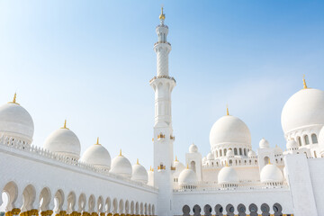 Minaret and domes of white Grand Mosque against white cloudy sky, also called Sheikh Zayed Grand...