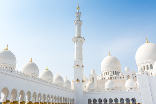 Minaret and domes of white Grand Mosque against white cloudy sky, also called Sheikh Zayed Grand Mosque, inspired by Persian, Mughal and Moorish mosque architecture