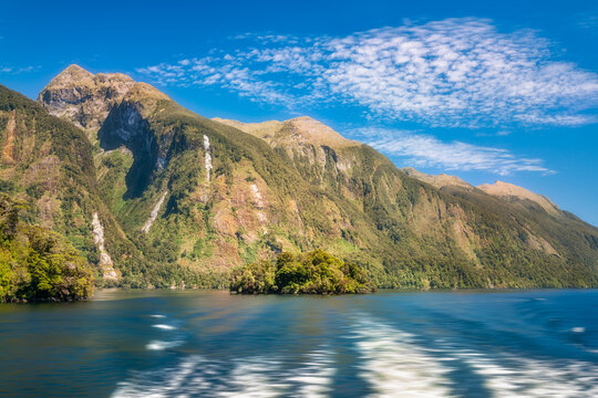 Spectacular mountain range perspective with the trail of the boat in the foreground on a beautiful summer day in the fjord at Doubtful Sound, New Zealand, South Island.