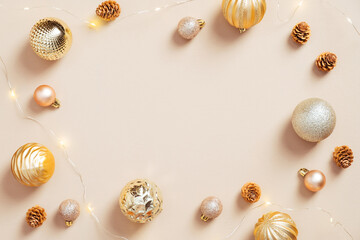 Minimal Christmas composition. Christmas frame border made of golden balls, cones, garland on pastel beige background. Glamour, fashion style. Flat lay.