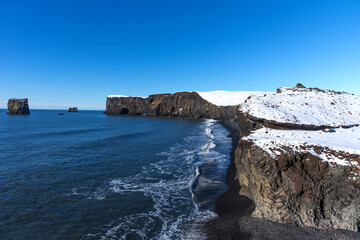 Aerial winter landscape view of Dyrholaey, Iceland.  Beautiful winter view of picturesque peninsula with black sand beach, lighthouse and large arch of volcanic rocks in the ocean.