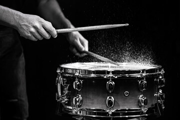 Drum sticks hitting snare drum with splashing water on black background under studio lighting. Black and white. Close up.