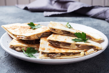 Pieces of quesadilla with mushrooms sour cream and cheese on a plate with parsley leaves. Concrete background close up.