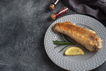 Fried fish hake Pollock and slices of fresh lemon. Dark concrete background. Copy space.
