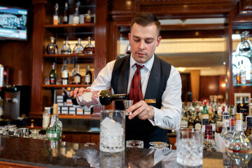 Bartenders do it better. Young bartender standing at counter and pouring red wine to prepare iced cocktail in the bar