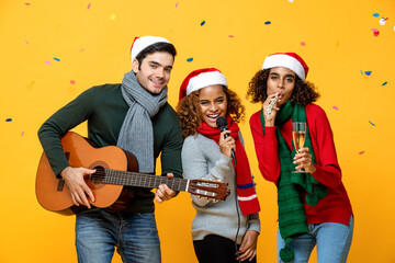 Happy diverse friends having party singing and celebrating Christmas in yellow studio background with colorful confetti