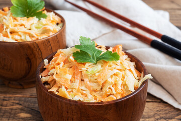 Salad of fresh grated carrots and green radish with sauce. Wooden table and dishes.