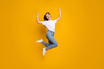 Full length body size photo of young girl fan jumping high gesturing like winner isolated on vibrant yellow color background