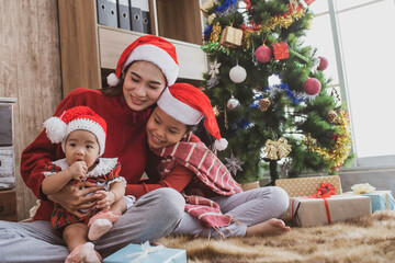 parent and two little children having fun and playing together near christmas tree indoors. merry christmas and happy holidays. cheerful mom and her cute daughters girls exchanging gifts.