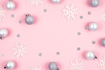 Top view of Christmas background made of silver decorations  balls and white snowflakes over pastel pink. Happy New Year greetings. Festive winter holidays backdrop. Flat lay. Copy space.