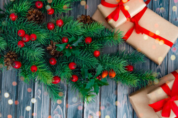 Decorated branches of a Christmas tree, cones, red berries and gifts on a wooden table. Christmas decor.