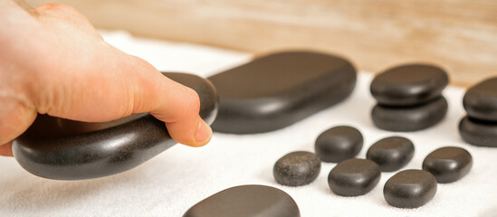 Hand of masseur lays out massage stones on the table in spa salon