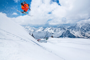 Professional athlete skier freerider in an orange suit with a backpack flies in the air after jumping on the lags on the background of blue sky and snow