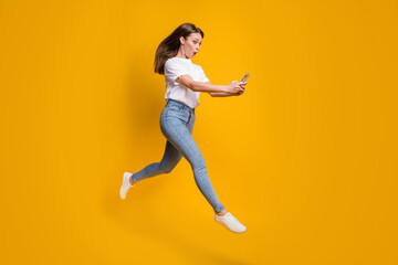 Fototapeta na wymiar Full length body size photo of amazed female influencer jumping reading on smartphone isolated on vivid yellow color background