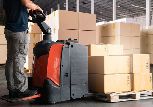 Warehouse worker working with electric forklift pallet jack unloading package boxes on pallet at the warehouse.Cargo shipment boxes, Packaging, Warehousing storage.