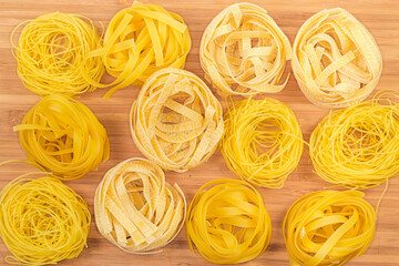 Different uncooked pasta nests on wooden cutting board, top view