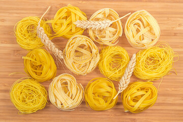 Different uncooked pasta nests and wheat ears on cutting board