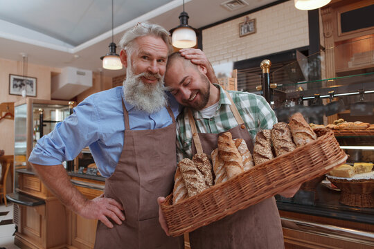 Happy proud senior male baker hugging his son, working together at bakery store