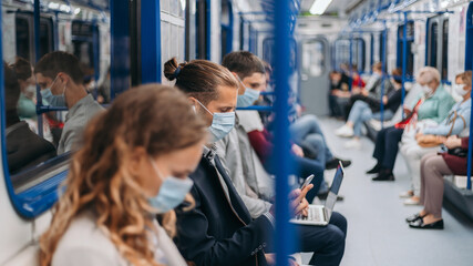 passengers in protective masks using their gadgets in the subway car .