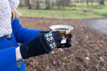 Hand of woman with gloves and cup of coffee in hands in autumn park
