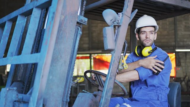 Concentrated forklift caucasian driver operating machine and holding hand on steering wheel  radio comminication operate teamwork with transportation of goods cargo in factory warehouse workshop.