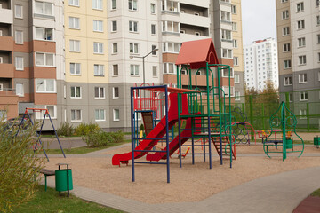 Fototapeta na wymiar A beautiful bright new playground with slides and staircases among tall high-rise buildings.