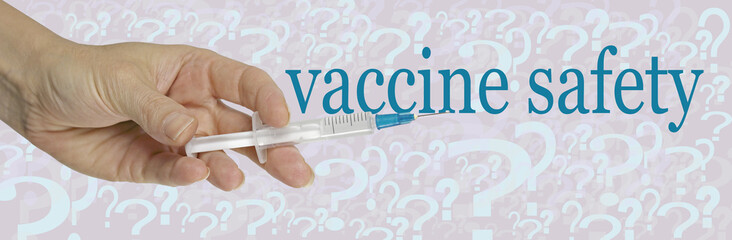 The Question of Vaccine Safety - hand holding a single dose syringe against a pale background with scattered multi-sized question marks and the words VACCINE SAFETY regarding COVID-19
