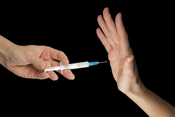 Thanks but I don't want your vaccine - hand holding a vaccine syringe opposite a hand in NO position against black background with copy space
