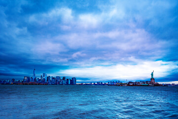 The Statue of Liberty over the New York cityscape at the evening dusk and cloudy weather