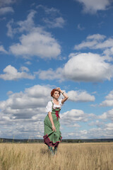 red haired woman in a Bavarian folk costume is standing in the field on the grass, oktoberfest