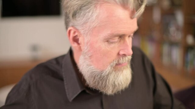 close-up of the face of a solid bearded gray-haired man who plays the piano at home
