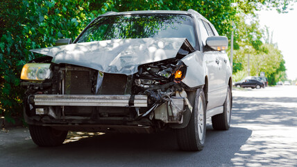 Destroyed car in car crash traffic accident on city road. Smashed broken front auto headlight, dented hood without bumper on gray car accident. Auto life health insurance.