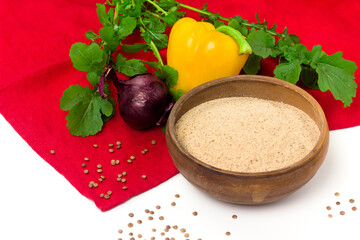 Red lentil whole grain flour in ceramic bowl and fresh vegetables on table cloth. Organic agriculture concept