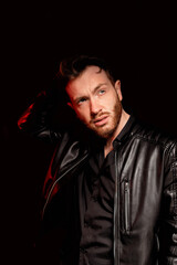 A brutal man on a dark background in the light of a red lamp.Black leather jacket