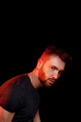 A brutal man on a dark background in the light of a red lamp.