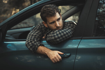 Young man with light skin and light eyes posing leaning out of the car window sticking his arms out...