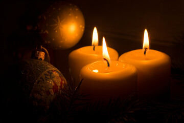 White candles with Christmas tree branches and Christmas tree toys on a dark background. The candle flame gives a sense of celebration and waiting for a gift. Holiday fairy-tale greeting card