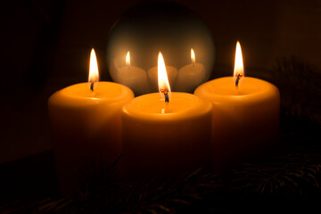 White candles with Christmas tree branches and Christmas tree toys on a dark background. The candle flame gives a sense of celebration and waiting for a gift. Holiday fairy-tale greeting card