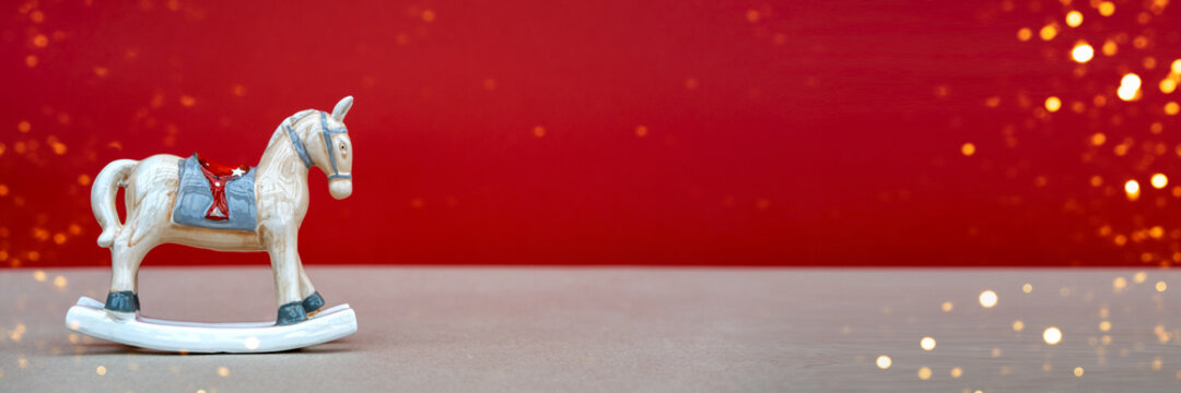 Christmas toy horse on red background with blurred lights. Copy space. Holiday christmas concept. Banner.