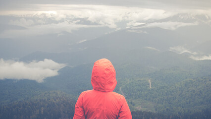 Girl in a red jacket looks at the mountains, back view
