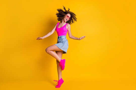 Full body photo of attractive youngster curly lady dance disco students party skinny figure wear sun specs pink tank top denim mini skirt shoes isolated vivid bright yellow color background