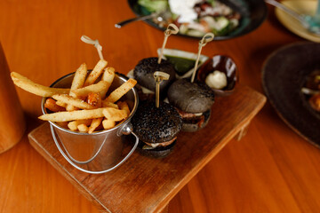 Delicious mini black burgers with beef, tomato, cheese served with french friesin basket on wooden table