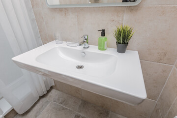 Close up of a beautiful snow-white sink with soap, an artificial flower and glassware in a matte bathroom of the hotel